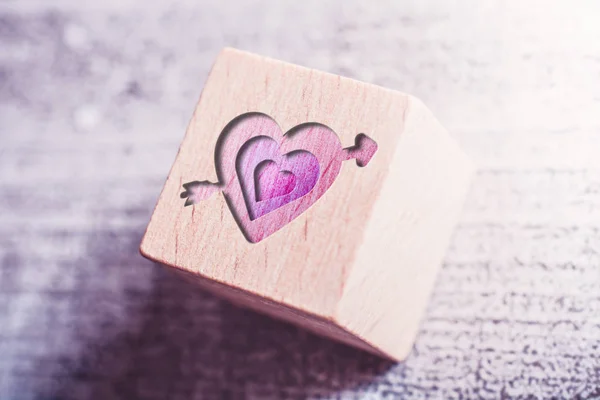 3 corazones rosados perforados por una flecha de Cupido grabada en un bloque de madera en una mesa — Foto de Stock