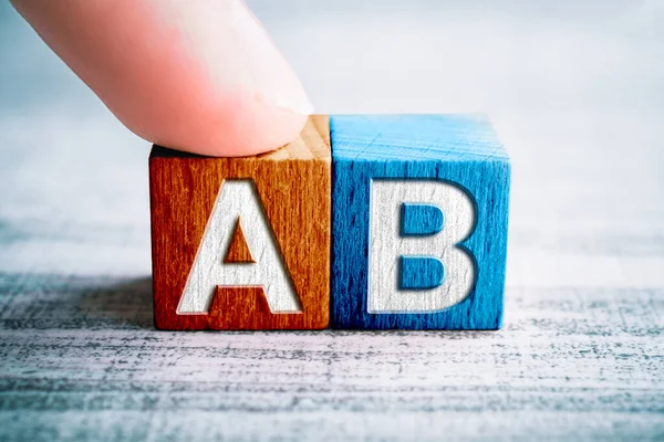 Escolha A e B em blocos de madeira em uma mesa, um dedo toca bloco A — Fotografia de Stock