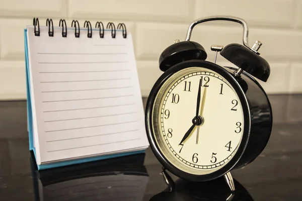 Reloj despertador y hoja en blanco del cuaderno sobre la mesa —  Fotos de Stock