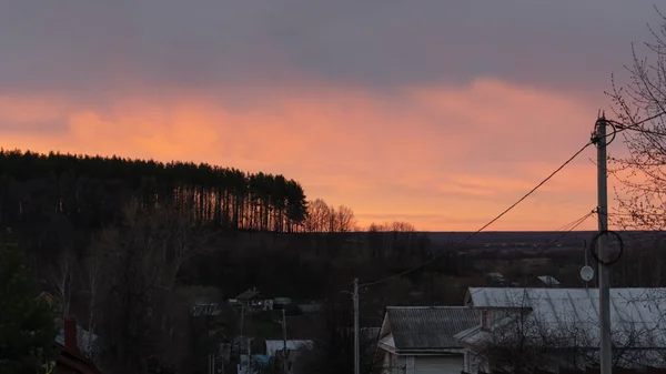 Red sunset on the background of a hill, houses descend to the bottom of the road. There is a spruce forest on the hill