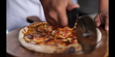 Pizza kesicisiyle pizzayı dilimleyen kişinin yavaş çekim yakın çekimi.