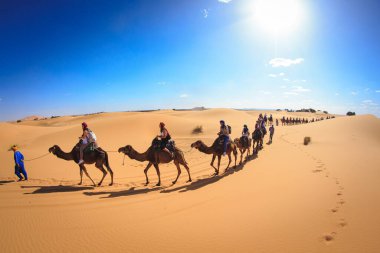Merzouga, Fas, Afrika; 29 Nisan 2018: Kum tepelerinin üzerinde gün batımı ve Sahra Çölü 'nde deveye binen insanlar, Fas, Afrika.