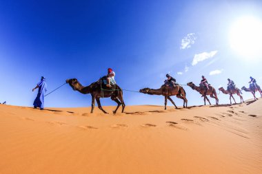 Merzouga, Fas, Afrika; 29 Nisan 2018: Kum tepelerinin üzerinde gün batımı ve Sahra Çölü 'nde deveye binen insanlar, Fas, Afrika.