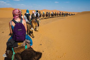 Kum tepelerinin üzerinde gün batımı ve Sahra Çölü 'nde deveye binen insanlar yolculukları sırasında, Fas, Afrika.