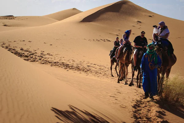 Merzouga, Fas, Afrika; 29 Nisan 2018: Kum tepelerinin üzerinde gün batımı ve Sahra Çölü 'nde deveye binen insanlar, Fas, Afrika.