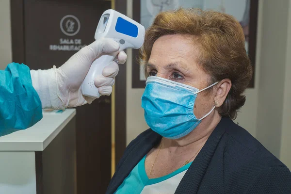 Fizyoterapi seansından önce hastanın ateşini ölçen bir profesyonel. Hastanın ve profesyonelin maskeleri ve koruyucu eldivenleri var. Covid 19 'dan kaçınmak için hijyen önlemleri..
