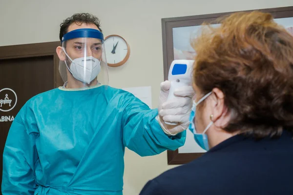 A professional taking the patient's temperature before the physiotherapy session. The patient and the professional have masks and protective gloves. Hygiene measures to avoid the Covid 19.