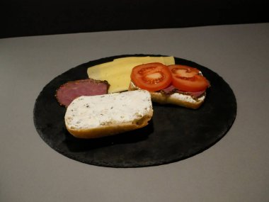 Siyah tabakta dilimlenmiş ekmek, peynir ve jambon.