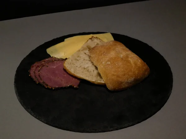 Scheibenbrot und Käse auf schwarzem Teller und grauem Hintergrund — Stockfoto