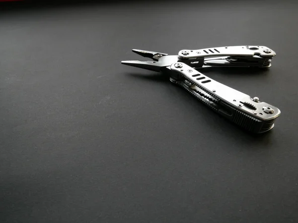 Multi tool with steel handles on a black paper background. Top view