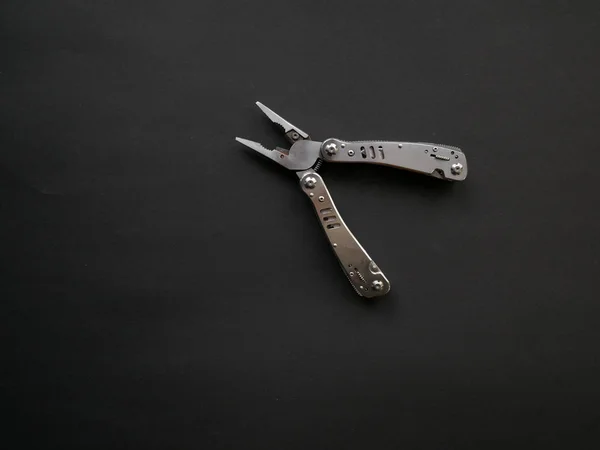 Multi tool with steel handles on a black paper background. Top view