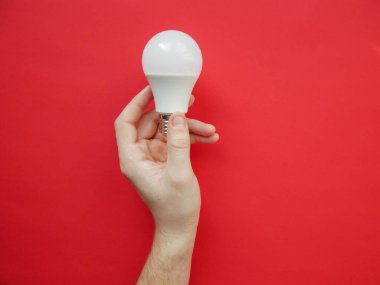 Kadın eli kırmızı arka planda bir LED lamba tutuyor. Enerji tasarrufu kavramı, alternatif enerji kaynakları, fikir. Boşluğu kopyala