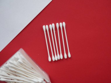 Kırmızı zemin üzerinde pamuk çubukları olan düz bir kompozisyon. Üst görünüm kulak çubukları.