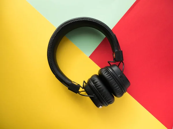 Classic black wireless headphones on colored paper background. Retro style. 80s. Pop culture. Top view. Minimal Music Concept