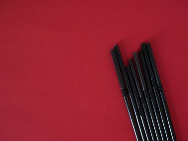 Kırmızı arkaplanda izole edilmiş siyah plastik pipetler.