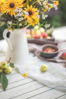 Elma ile masada bir vazoda sarı çiçekler