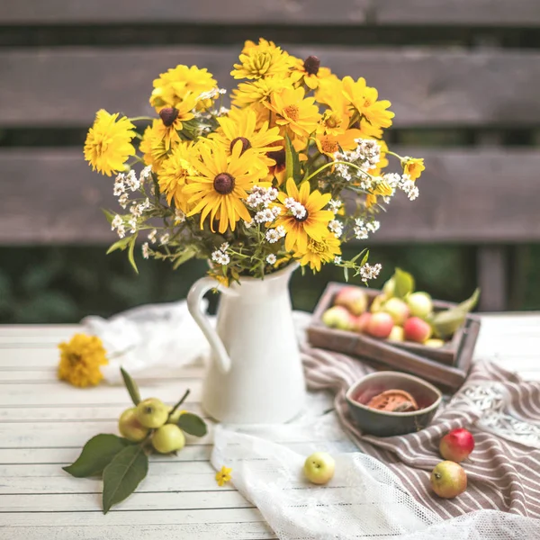 Flores amarillas en un jarrón sobre la mesa con manzanas — Foto de Stock