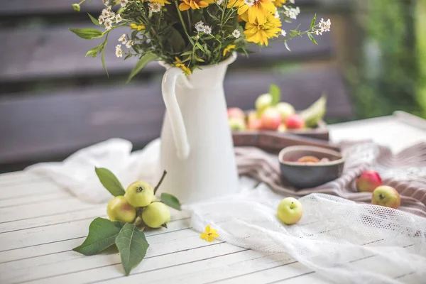 Желтые цветы в вазе на столе с яблоками — стоковое фото