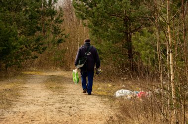 Bir balıkçı, ormanın etrafında bir sürü atıkla yürür.