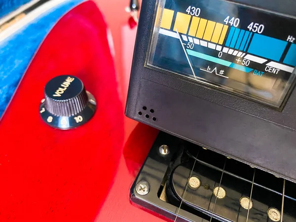 Detail of tuner with red electric guitar and volume button