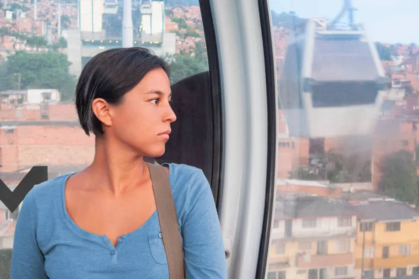 Mavi tişörtlü kadın, sonsuzlukta pencereden dışarı bakıyor. Medellin 'in yüksekliğinin üzerinde bir füniküler içinde.