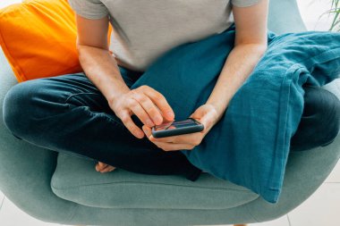 Evdeki akıllı telefonda turkuaz koltukta yalınayak yazan bir adam.