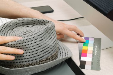 Adamın eli renkli bantları işaret ediyor, diğer elinde şapka var.