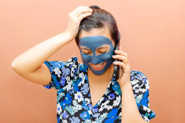 Mavi bir maske takan ve telefonda konuşan turuncu arka planda gülen bir kadın.