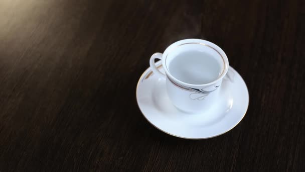 Sur la table se trouve une tasse blanche avec de l'eau bouillante. Sachet de thé noir brassé .