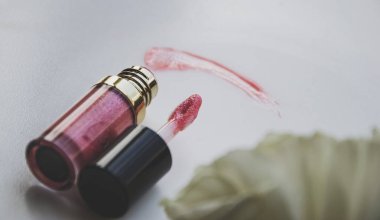 Makyaj için pembe ruj. Dudakları simli pastel merhemi. Arka planda beyaz fildişi çiçek var. Parlak efektli parlatıcı. Küçük kadın aksesuar. 