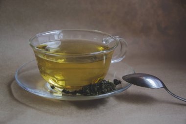 Kahverengi arka planda bir fincan yeşil çay, kuru yapraklar ve küçük yasemin çiçekleri. Resmini tazelemek için taze çayla kapat. Tatil için sağlıklı içecekler. Metal kaşık yan tarafta.. 