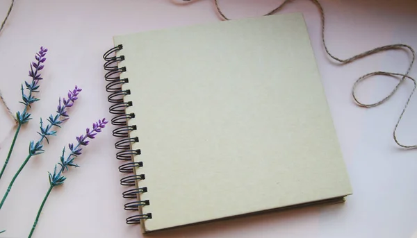 Brown spiral notebook on light background with lavender flowers and tread on the side. Copy space with empty place for text or picture. Office wallpaper in lavender shade. Tools for business.