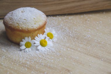Üstü beyaz pudralı ev yapımı çöreğin yakın plan resmi ve yanında da kahverengi ahşap arka planda bulunan küçük papatyalar yiyecek fotoğraf konseptinde metin için boş alan. 