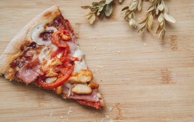 Pizza dilimini domatesli, tavuklu ve mantarlı yakın plan kahverengi ahşap arka plan ve yanında kuru yapraklar ve restoranda öğle yemeği için boş alan. 