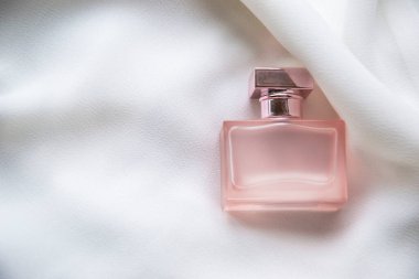 Fildişi beyazı ipek arka planda bulunan küçük pembe parfüm şişesinin resmini kapatıyoruz. Moda duvar kâğıdı olarak metin için yer ayırıyoruz. Cazibeli ürünler ve zarif hanımlara özen gösteriyoruz.