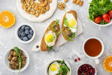 Sağlıklı kahvaltı ile kızarmış yumurta, taze ekmek, salata, çilek, domates, fındık, içecek Kupası, roka, gri hafif bir arka plan üzerinde mantar. Üstten Görünüm