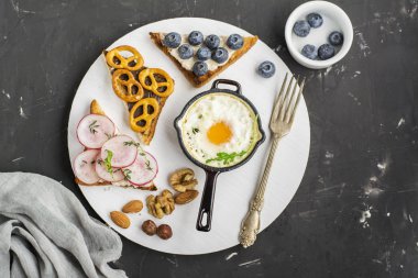 Lezzetli breakfast modern. Fıstık ezmesi, yaban mersini, turp simit kurabiye kurulu koyu arka plan üzerinde bir toplu iş dökme demir tava ve kızarmış ekmek tabağı kızarmış yumurta. Üstten Görünüm