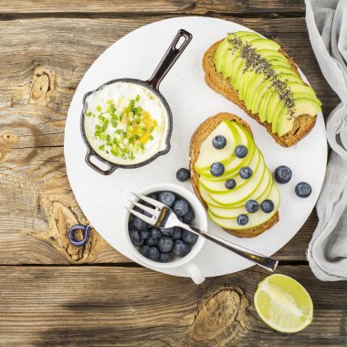 yumurta toplu tavada, basit bir ahşap zemin üzerine yeşil elma, avokado, taze yaban mersini ile tost lezzetli sağlıklı kahvaltı. Üstten Görünüm. Renk yıl. Yeşillik