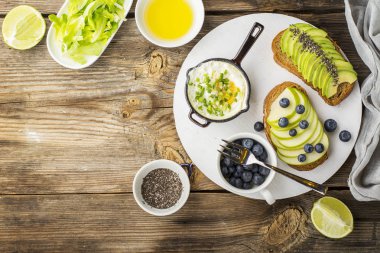 yumurta toplu tavada, basit bir ahşap zemin üzerine yeşil elma, avokado, taze yaban mersini ile tost lezzetli sağlıklı kahvaltı. Üstten Görünüm. Renk yıl. Yeşillik