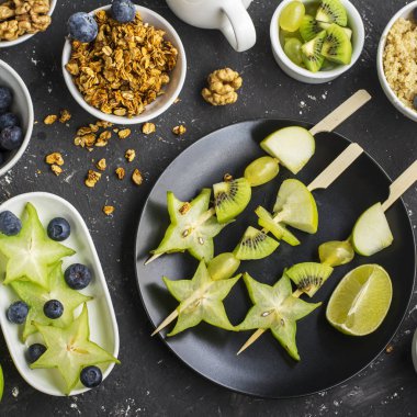 Sağlıklı taze kahvaltı. Granola, quinoa kase, çeşitli fındık ve meyve şişleri karanlık bir arka plan üzerinde yeşil meyve ile. Üstten Görünüm. Renk yıl. Yeşillik