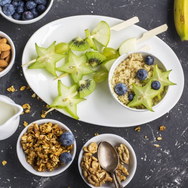 Sağlıklı taze kahvaltı. Granola, quinoa kase, çeşitli fındık ve meyve şişleri karanlık bir arka plan üzerinde yeşil meyve ile. Üstten Görünüm. Renk yıl. Yeşillik