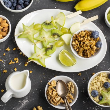 Sağlıklı taze kahvaltı. Granola, quinoa kase, çeşitli fındık ve meyve şişleri karanlık bir arka plan üzerinde yeşil meyve ile. Üstten Görünüm. Renk yıl. Yeşillik