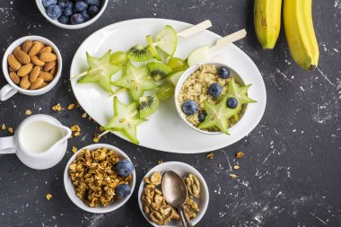 Sağlıklı taze kahvaltı. Granola, quinoa kase, çeşitli fındık ve meyve şişleri karanlık bir arka plan üzerinde yeşil meyve ile. Üstten Görünüm. Renk yıl. Yeşillik