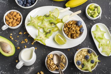 Sağlıklı taze kahvaltı. Granola, quinoa kase, çeşitli fındık ve meyve şişleri karanlık bir arka plan üzerinde yeşil meyve ile. Üstten Görünüm. Renk yıl. Yeşillik