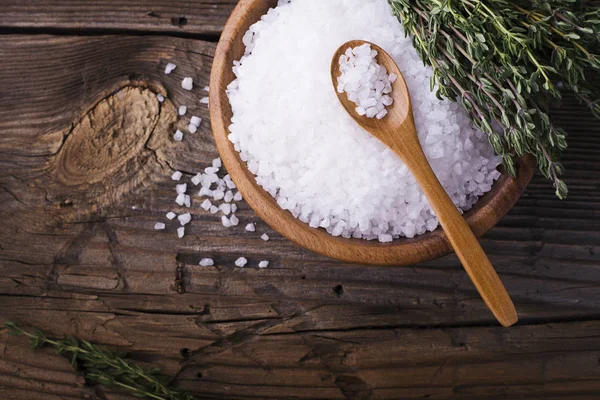 Large White sea salt in a natural wooden bowl with sprig of fresh rosemary on simple background. Selective focus. — Stock Photo, Image