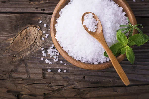Large White sea salt in a natural wooden bowl with  sprig of fresh rosemary on  simple  background. Selective focus. — Stock Photo, Image