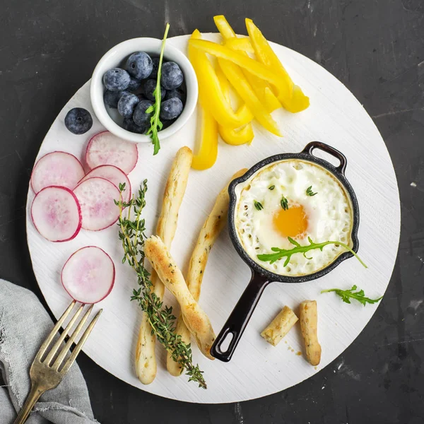 Œufs brouillés pour le petit déjeuner dans la poêle en fonte sur un tableau blanc avec baguettes en colère et légumes — Photo