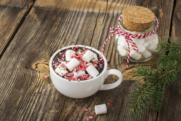 cup of fragrant homemade cocoa with marshmallows and crushed red white candy topping. On the simple wooden textural background. selective focus