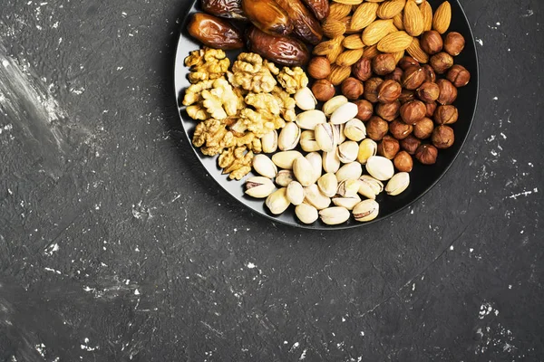 Ανάμεικτα καρύδια, αμύγδαλα, φιστίκια, καρύδια, φουντούκια και σύκα σε σκούρο φόντο μαύρο κεραμικό πιάτο. Το Top view — Φωτογραφία Αρχείου