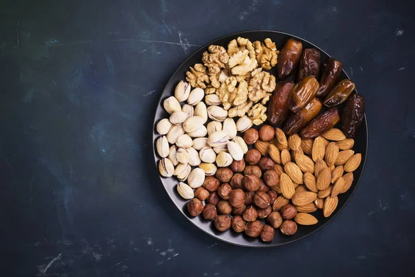 Ανάμεικτα καρύδια, αμύγδαλα, φιστίκια, καρύδια, φουντούκια και σύκα σε σκούρο φόντο μαύρο κεραμικό πιάτο. Το Top view — Φωτογραφία Αρχείου